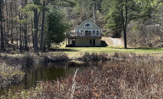 rear view of property with a yard, a view of trees, and a deck with water view