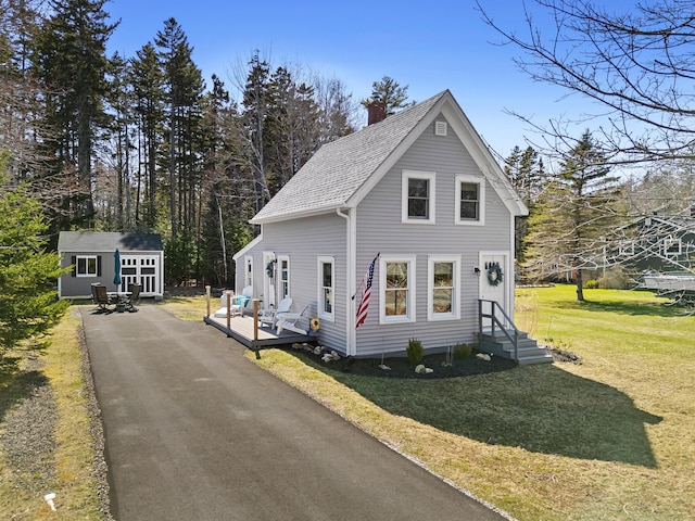 view of front of home featuring roof with shingles, a front lawn, a wooden deck, a chimney, and an outdoor structure