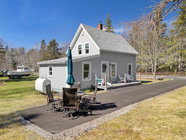 back of property featuring a shingled roof, heating fuel, a chimney, a patio, and a yard