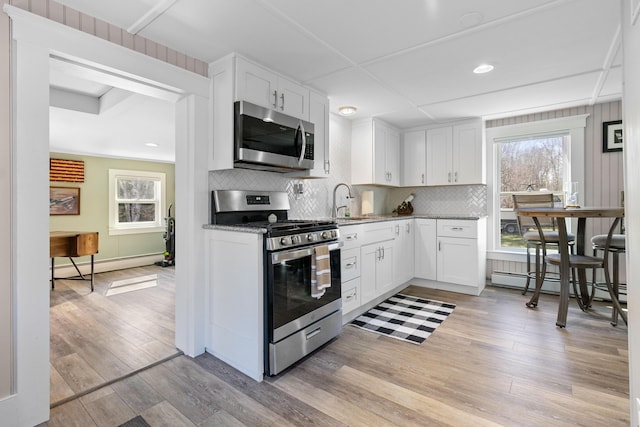kitchen with baseboard heating, light wood-type flooring, white cabinets, a baseboard radiator, and appliances with stainless steel finishes