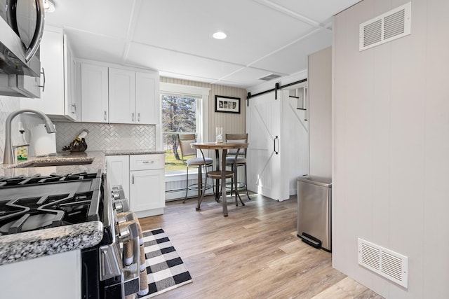 kitchen with visible vents, a barn door, light wood-style flooring, and white cabinets