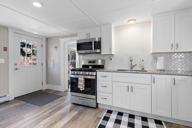 kitchen with decorative backsplash, a sink, stone countertops, white cabinets, and stainless steel appliances
