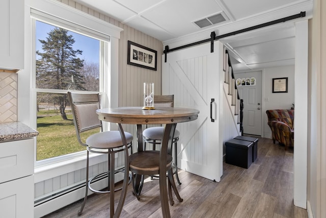 dining room featuring visible vents, wood finished floors, a healthy amount of sunlight, baseboard heating, and a barn door