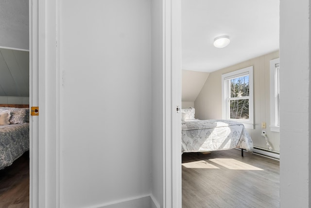 bedroom featuring a baseboard heating unit, wood finished floors, and lofted ceiling