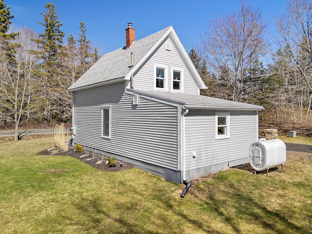 view of home's exterior featuring a lawn, heating fuel, a chimney, and roof with shingles