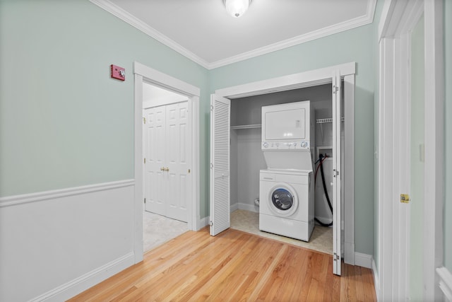 laundry room with wood finished floors, laundry area, ornamental molding, stacked washing maching and dryer, and baseboards