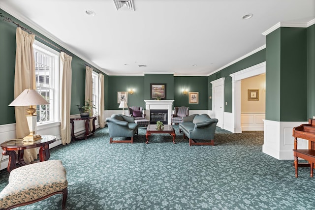 carpeted living area featuring baseboard heating, ornamental molding, a glass covered fireplace, visible vents, and a wainscoted wall