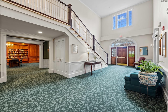 carpeted entrance foyer featuring stairs, a wainscoted wall, crown molding, and a towering ceiling