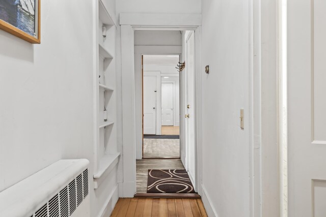 hall with built in shelves, light wood-style flooring, and radiator