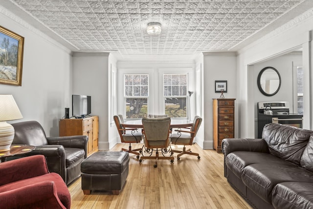 living area featuring an ornate ceiling, ornamental molding, baseboards, and light wood-style flooring