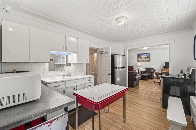 kitchen featuring light wood-style floors, freestanding refrigerator, white cabinetry, white microwave, and ornamental molding