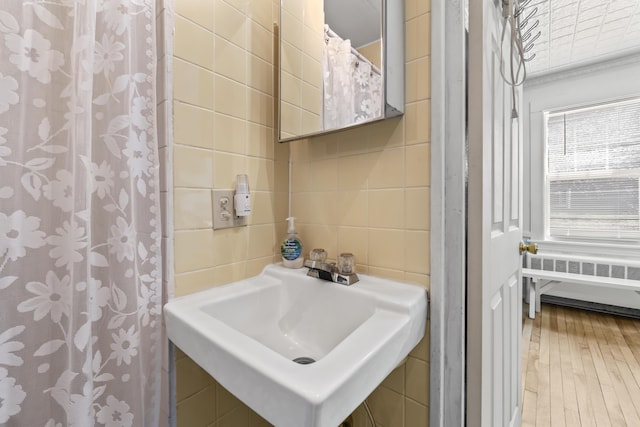 bathroom featuring radiator heating unit, tile walls, wood finished floors, and a sink