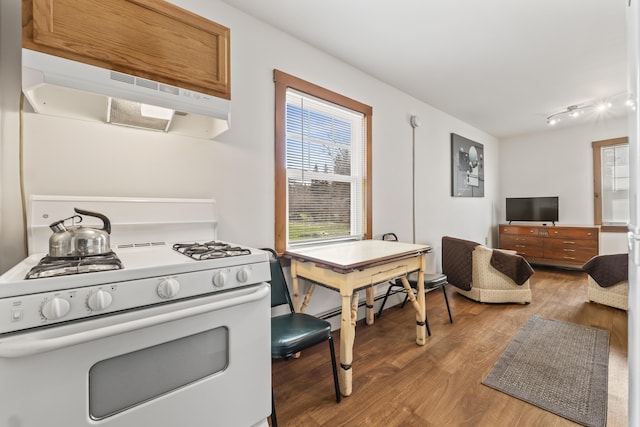 kitchen featuring white range with gas stovetop, brown cabinets, wood finished floors, and under cabinet range hood