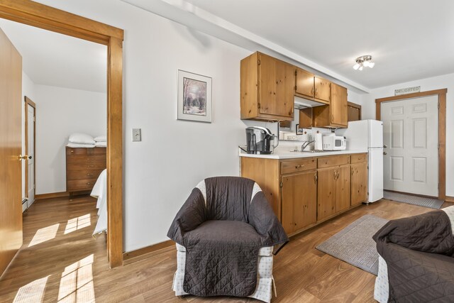 kitchen with a sink, white appliances, light countertops, light wood-style flooring, and baseboards