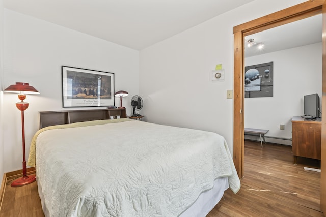 bedroom with wood finished floors, baseboards, and a baseboard heating unit