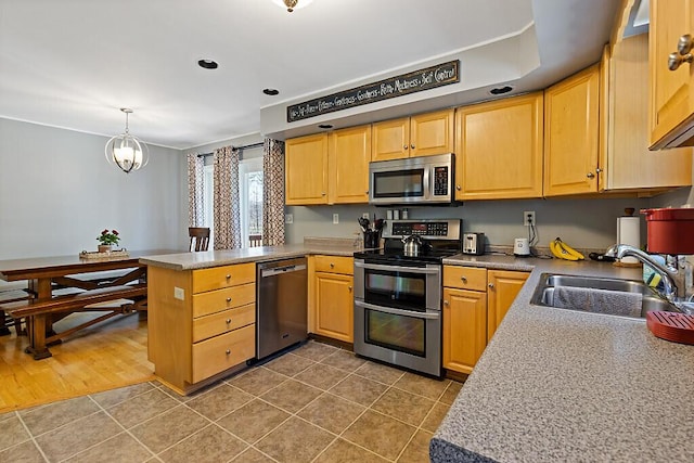 kitchen featuring a peninsula, dark tile patterned flooring, a sink, appliances with stainless steel finishes, and decorative light fixtures