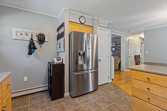 kitchen with light brown cabinetry, baseboards, stainless steel fridge, a baseboard heating unit, and dark tile patterned flooring