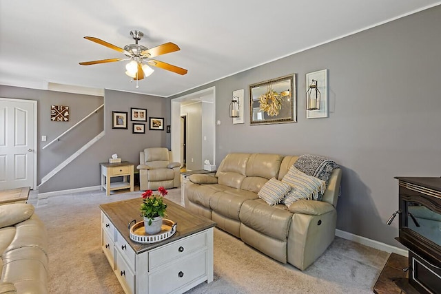 living area featuring ceiling fan, light colored carpet, a wood stove, stairway, and baseboards