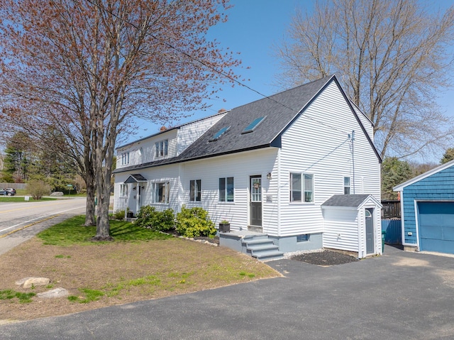 view of front facade featuring roof with shingles, a storage shed, central AC unit, an outdoor structure, and driveway