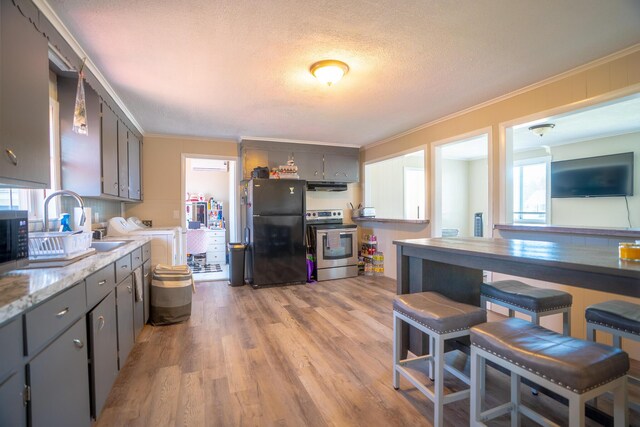 kitchen with ornamental molding, under cabinet range hood, light wood-style flooring, gray cabinetry, and stainless steel appliances
