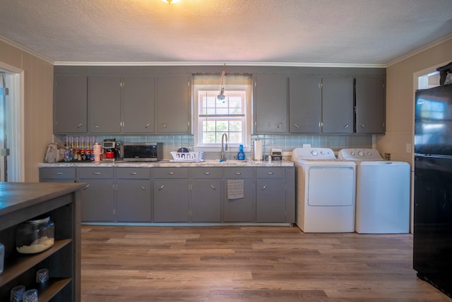 kitchen with gray cabinetry, ornamental molding, washer and clothes dryer, and wood finished floors