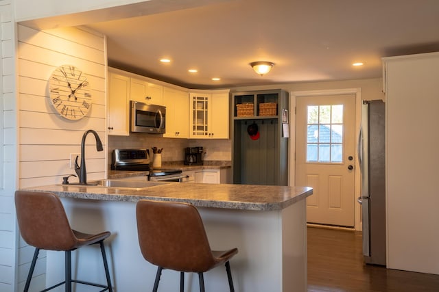 kitchen featuring dark wood-style flooring, a peninsula, glass insert cabinets, a sink, and appliances with stainless steel finishes