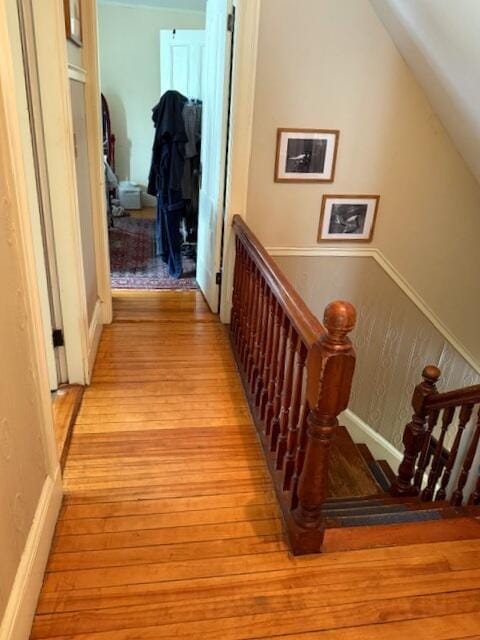 corridor with vaulted ceiling, an upstairs landing, a wainscoted wall, and wood finished floors