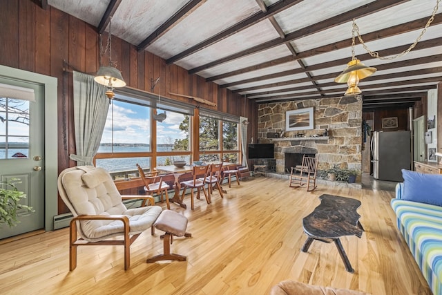 living area featuring wood-type flooring, wood walls, a stone fireplace, beamed ceiling, and a baseboard heating unit