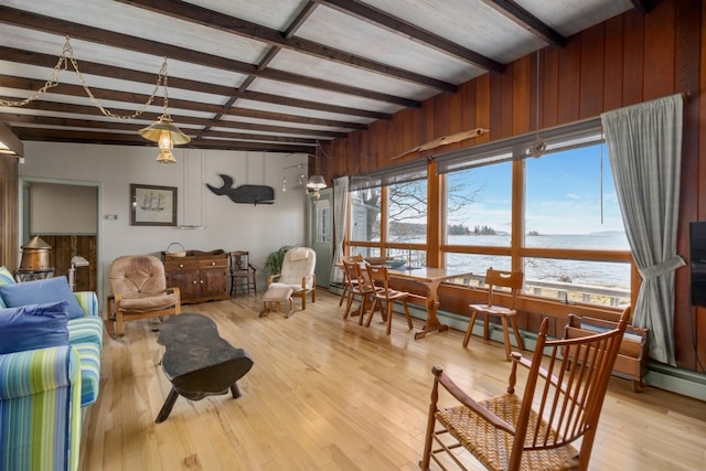 living area with light wood-style floors, a water view, beamed ceiling, and wooden walls