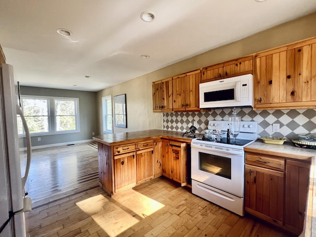 kitchen with white appliances, a peninsula, backsplash, light wood-type flooring, and recessed lighting
