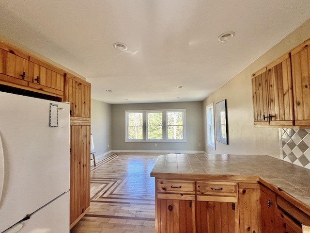 kitchen with freestanding refrigerator, a peninsula, tile countertops, brown cabinetry, and recessed lighting