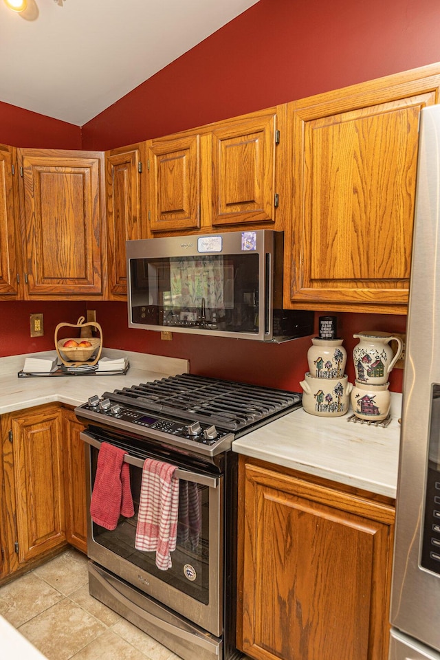 kitchen featuring stainless steel appliances, lofted ceiling, light countertops, brown cabinetry, and light tile patterned floors