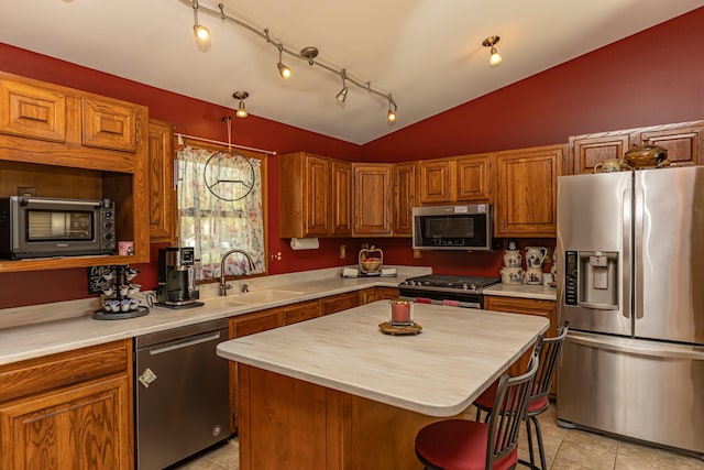 kitchen featuring appliances with stainless steel finishes, vaulted ceiling, a sink, brown cabinets, and a center island