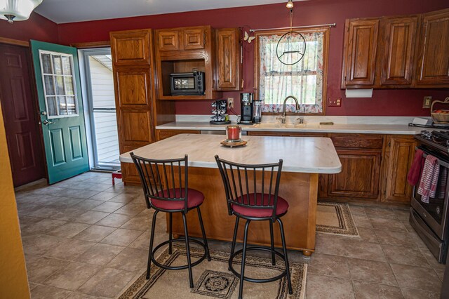 kitchen with stainless steel gas range, light countertops, a center island, a breakfast bar area, and a sink