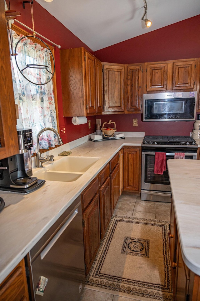 kitchen featuring stainless steel appliances, a sink, light countertops, lofted ceiling, and light tile patterned floors