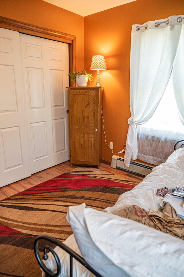 bedroom featuring a baseboard heating unit, a closet, and light wood-style floors