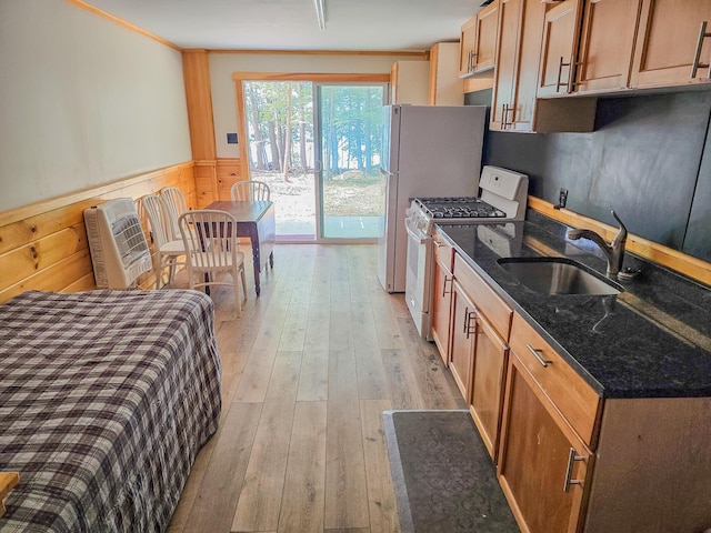kitchen featuring wainscoting, a sink, light wood-style flooring, dark stone counters, and white range with gas stovetop
