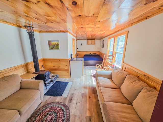 living area with a wood stove, wainscoting, hardwood / wood-style flooring, wood walls, and wooden ceiling
