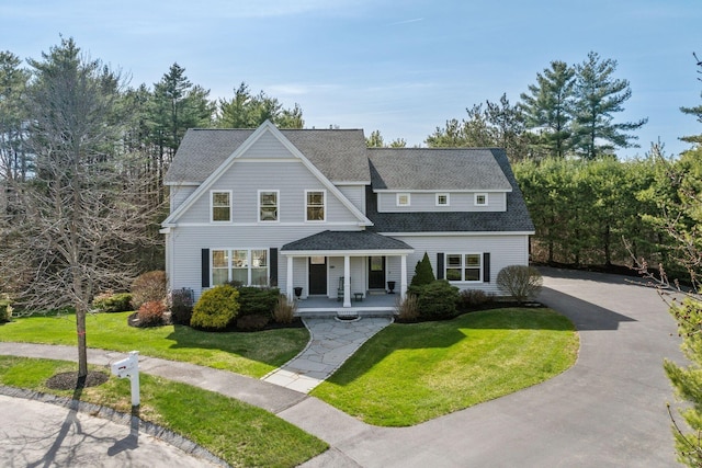 shingle-style home with covered porch, a shingled roof, a front yard, and aphalt driveway