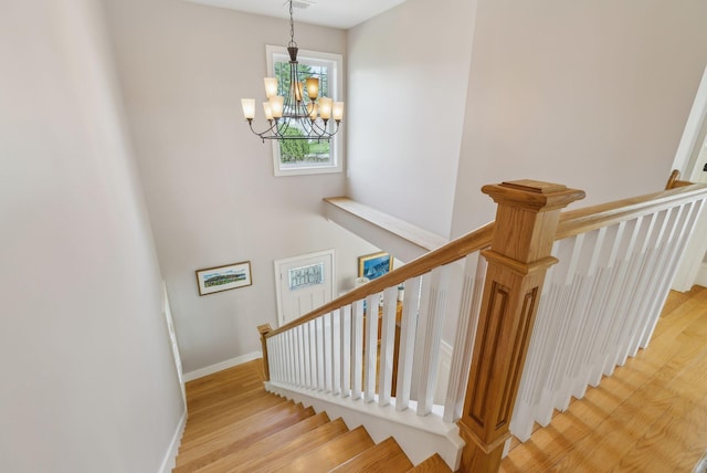 stairs featuring an inviting chandelier, baseboards, and wood finished floors