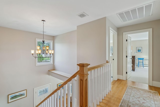 hall with a notable chandelier, visible vents, light wood finished floors, and an upstairs landing