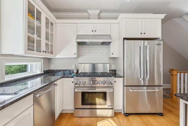 kitchen with dark stone counters, white cabinetry, under cabinet range hood, and stainless steel appliances