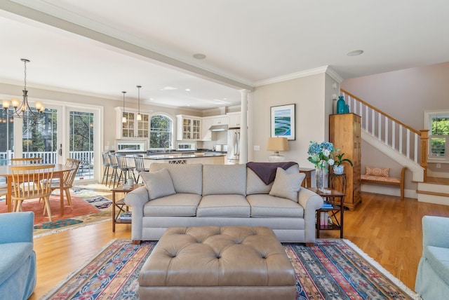 living area with a notable chandelier, plenty of natural light, stairway, and light wood-style floors