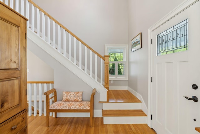 entrance foyer featuring stairway, baseboards, light wood-style flooring, and a towering ceiling