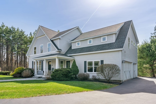 shingle-style home with a front yard, a shingled roof, an attached garage, driveway, and a porch