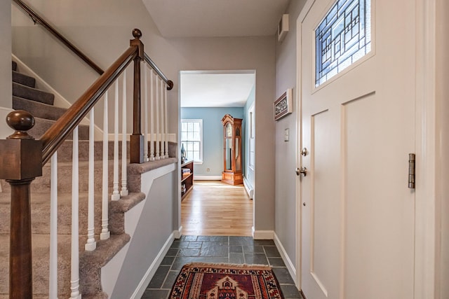 foyer entrance featuring stone tile flooring, baseboards, a baseboard heating unit, and stairway