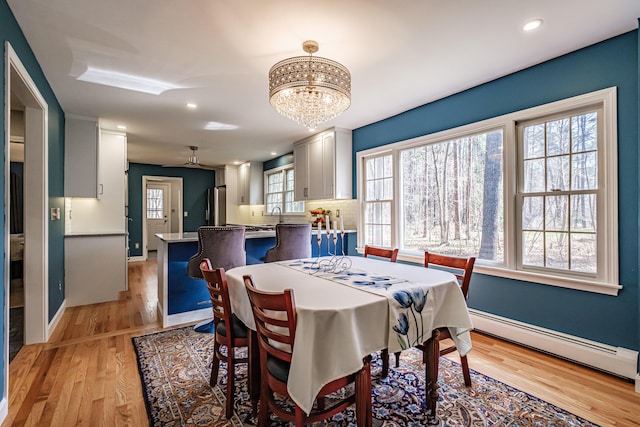 dining area featuring baseboards, light wood finished floors, a notable chandelier, and baseboard heating