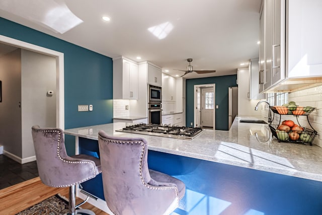 kitchen with appliances with stainless steel finishes, tasteful backsplash, a sink, white cabinets, and recessed lighting