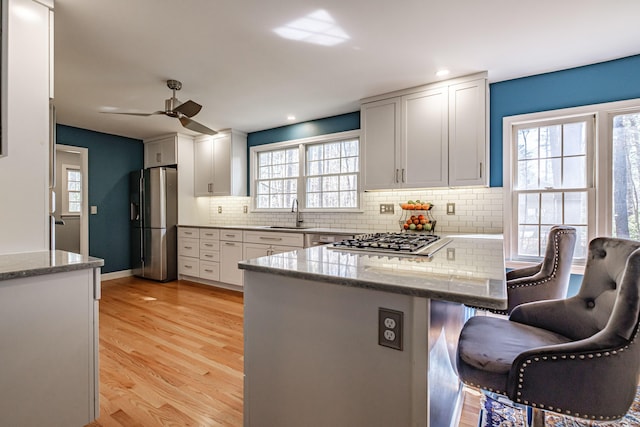 kitchen featuring a ceiling fan, appliances with stainless steel finishes, white cabinets, a peninsula, and a breakfast bar