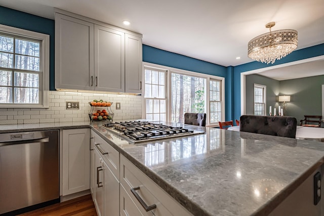kitchen with backsplash, appliances with stainless steel finishes, dark stone countertops, open floor plan, and an inviting chandelier